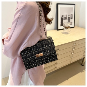 Detail of black tweed crossbody bag with gold hardware lock and chain strap on shoulder