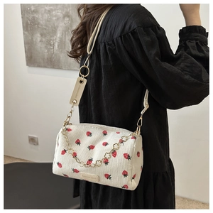 Close-up of strawberry print corduroy shoulder bag with gold floral chain and leather tag