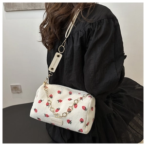 Detail of white corduroy shoulder bag featuring red strawberry embroidery and golden chain
