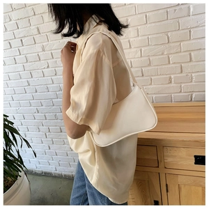 Detailed view of a creamy white minimalist underarm bag worn over the shoulder by a model