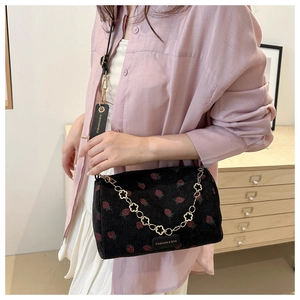 Detail of strawberry print corduroy bag with golden floral chain and leather strap