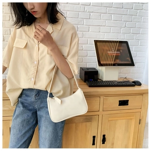 Close-up of minimalist white underarm bag styled with yellow shirt and blue jeans