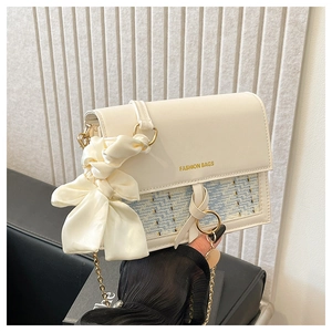 Detail of tweed flap bag with gold chain strap and large white satin bow accessory
