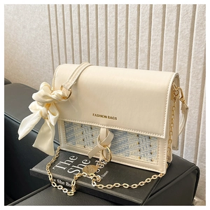 Detail of cream crossbody bag with tweed texture, silk bow, and gold chain strap