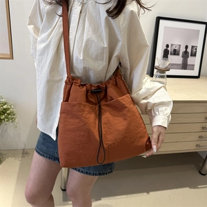 Fashionable rust orange nylon drawstring bucket bag with adjustable shoulder strap for women