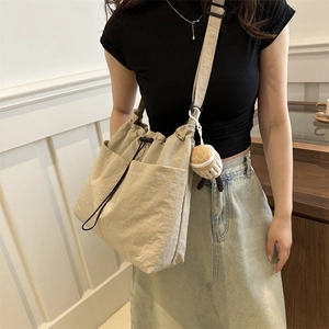 Beige nylon drawstring bucket bag with adjustable black strap and cute plush charm