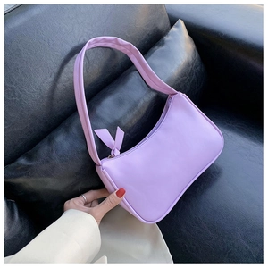 Close-up of lavender PU leather underarm bag with bow decoration on black sofa