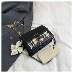 Detail of tweed and leather flap bag with gold chain and silk bow accent beside a phone