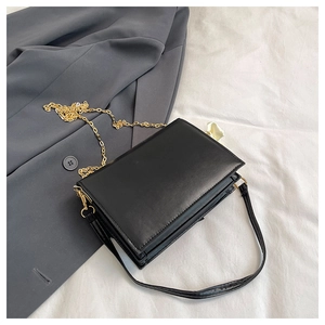 Close-up of black rectangular shoulder bag with gold chain and matte leather texture