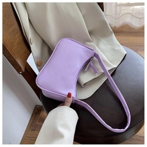 Detail of light purple PU leather baguette bag with wide strap on leather surface