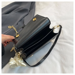 Detail view of black leather crossbody bag with dual compartments and gold chain strap