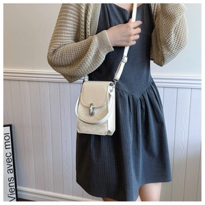 Model wearing a cream white leather crossbody bag with silver twist lock in a home setting