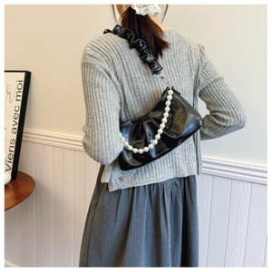 Detail of black pleated crescent bag featuring pearl strap and satin shoulder handle