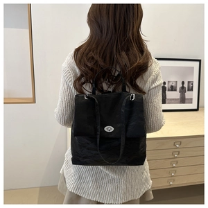 Close-up of minimalist black pleated backpack with metallic twist lock on female model
