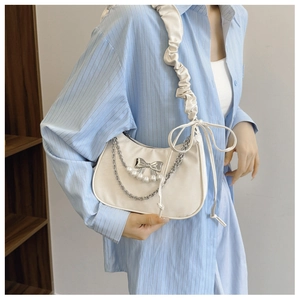 Detail of cream pleated shoulder bag with pearl chain and silver bow charm on model