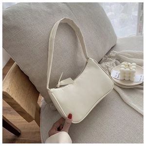 Creamy white leather baguette shoulder bag shown in a cozy home setting with candles