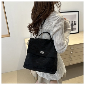 Detail of black pleated fabric texture and silver twist lock on woman's backpack