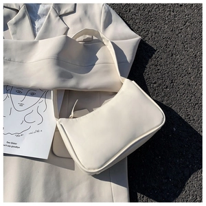 Close-up of a minimalist cream PU leather baguette bag on a beige blazer background