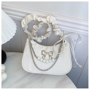 Detail of white dumpling bag with silver bow charm, pearl chain, and ruched handle strap