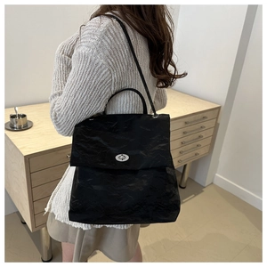 Détail du fermoir rotatif argenté et texture plissée sur un sac à bandoulière noir