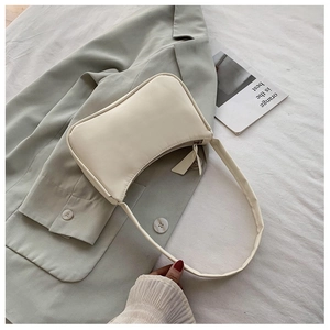 Detail of minimalist beige leather underarm bag with silver zipper on grey blazer