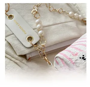 Détail du fermoir mousqueton doré et de la chaîne en perles sur le sac cylindrique