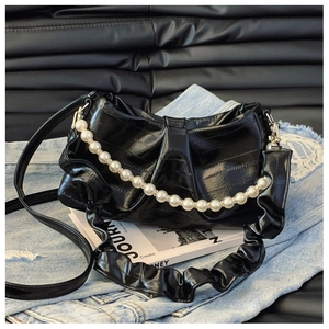 Detail of black glossy handbag featuring pearl chain decoration and pleated surface