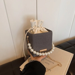 Deep grey mini bucket bag with pearl handle and gold chain strap on a book background