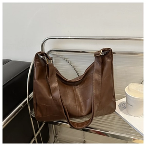 Detail of a brown vintage tote bag featuring a textured patchwork design and gold metal hardware