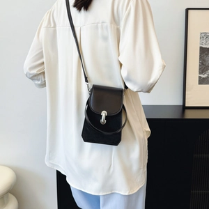 Mini sac bandoulière noir en cuir minimaliste avec boucle en U argentée sur un modèle