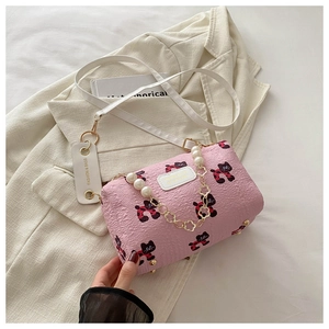 Detail der rosa Zylindertasche mit Katzenprints und Perlenkette auf beige Sakko Hintergrund