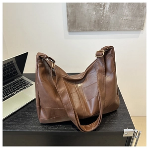Detail view of large dark brown leather tote bag with rectangular stitching on office desk