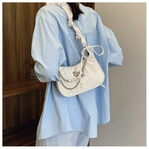 Detail of white dumpling shoulder bag featuring pearl chains and bow charm on a model