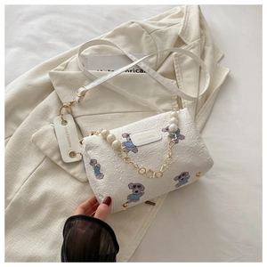 Detail der weißen zylindrischen Umhängetasche mit blauem Hundeprint und Perlenkette