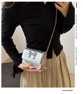 Detail of silver flap crossbody bag featuring a 3D metallic bow and slim chain strap