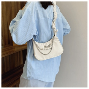 Close-up of white crescent bag with pearl chain and ruffled strap worn by model