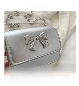 Detail of silver crossbody bag with metallic bow clasp and fine chain strap