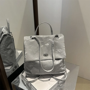 Silver metallic backpack with crinkled texture and sleek metal clasp on a minimalist base
