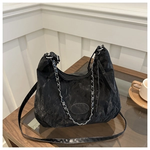 Close-up of black pleated crossbody bag with silver chain detail on a glass table