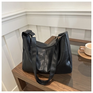 Close-up of minimalist black leather patchwork shoulder bag with golden metal hardware