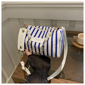 Makroaufnahme der blau gestreiften Zylindertasche mit Perlenkette und modischem Etikett