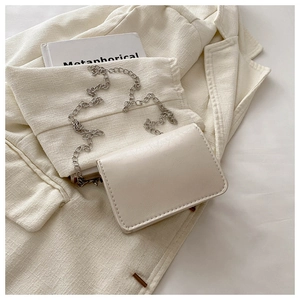 Detail of cream white leather crossbody bag with metal chain strap and flap closure