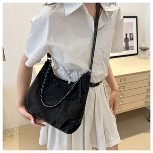 Close-up of black pleated shoulder bag with silver chain worn by a model in a cozy room