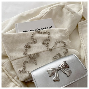 Detail of silver mini crossbody bag featuring a 3D mirror bow and metallic pleated texture