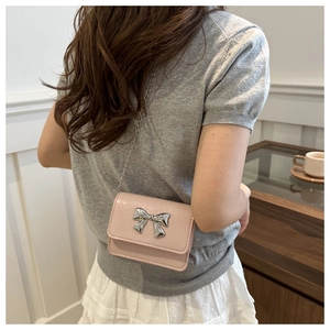 Detail of pink patent leather crossbody bag with silver bow and delicate chain strap
