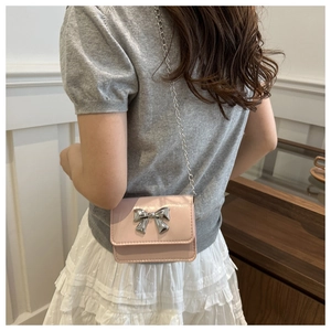Detail of pink crossbody bag with silver butterfly clasp and chain strap on model