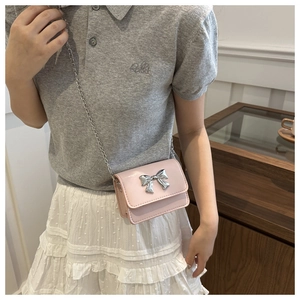 Detail of pink patent leather crossbody bag with silver bow and chain strap