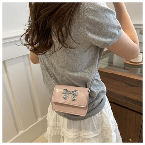 Detailed macro view of pink patent leather mini bag with silver bow accent and chain strap