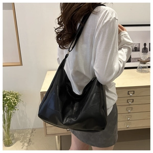 Close-up of minimalist black tote bag with textured patchwork details and long shoulder strap