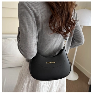 Détail d'un sac porté épaule croissant noir avec logo doré sur un mannequin élégant
